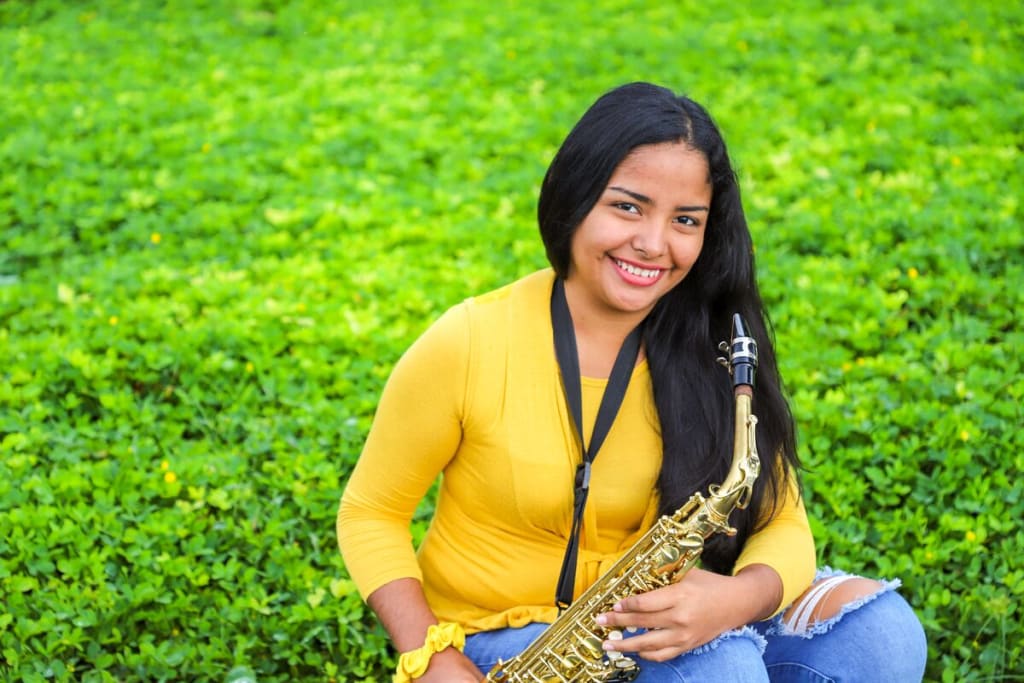 Dennisis wears a bright yellow sweater and holds a saxophone